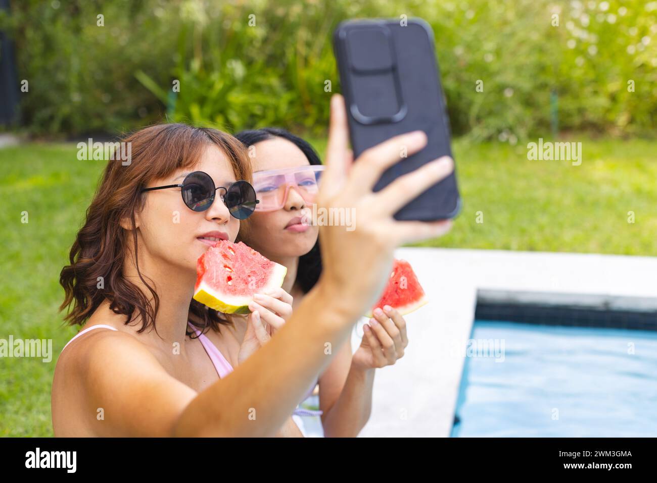 Due giovani donne birazziali si godono una giornata di sole a bordo piscina, scattando un selfie Foto Stock