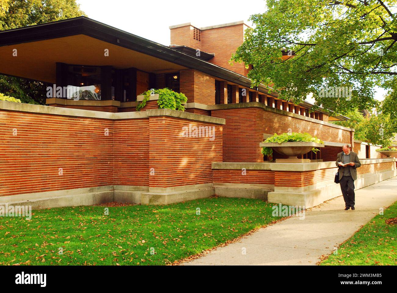 Un uomo adulto legge un libro mentre passa davanti alla Robie House progettata da Frank Lloyd Wright a Chicago Foto Stock