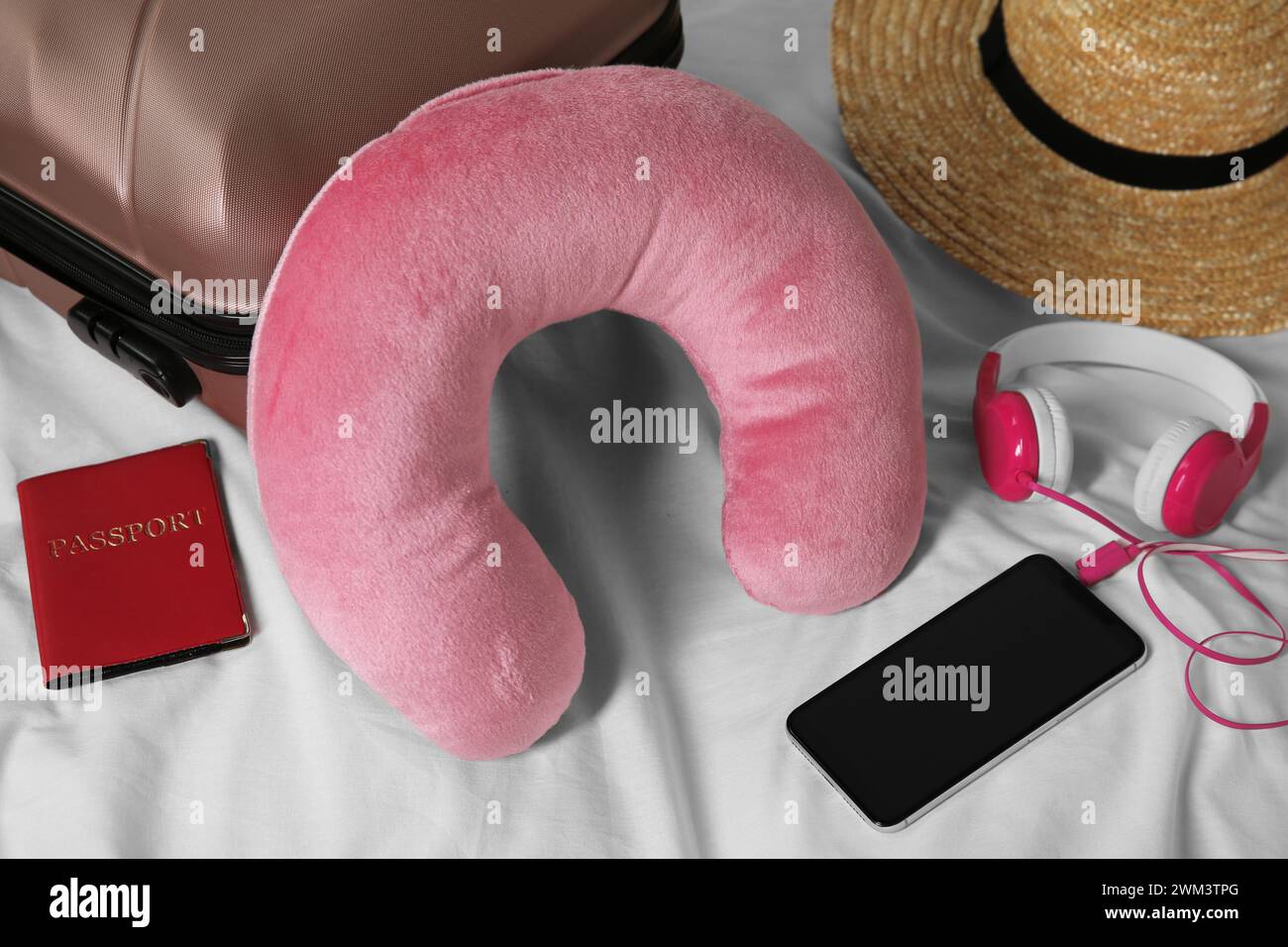 Cuscino da viaggio rosa, valigia, smartphone con cuffie e passaporto sul letto Foto Stock