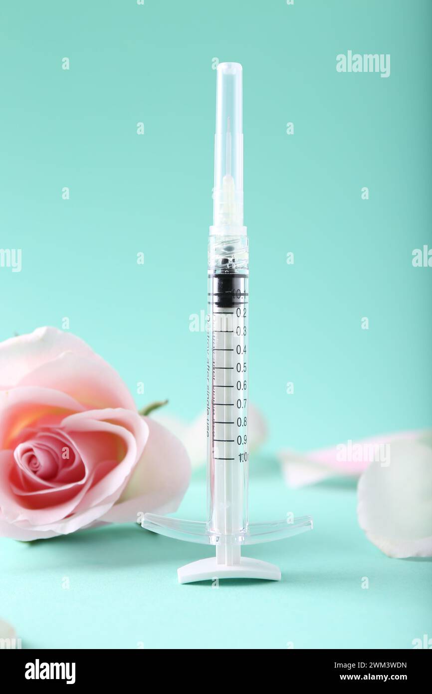 Cosmetologia. Siringa medica, fiore di rosa e petali su sfondo turchese Foto Stock