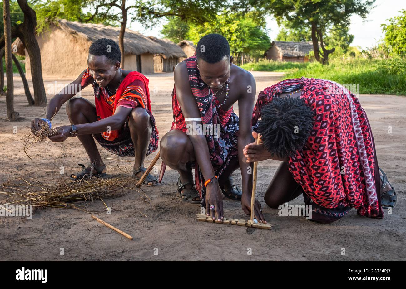 Due guerrieri Maasai usano l'attrito sfregando i bastoncini insieme per accendere un fuoco in un villaggio di Mikumi, Tanzania. Foto Stock