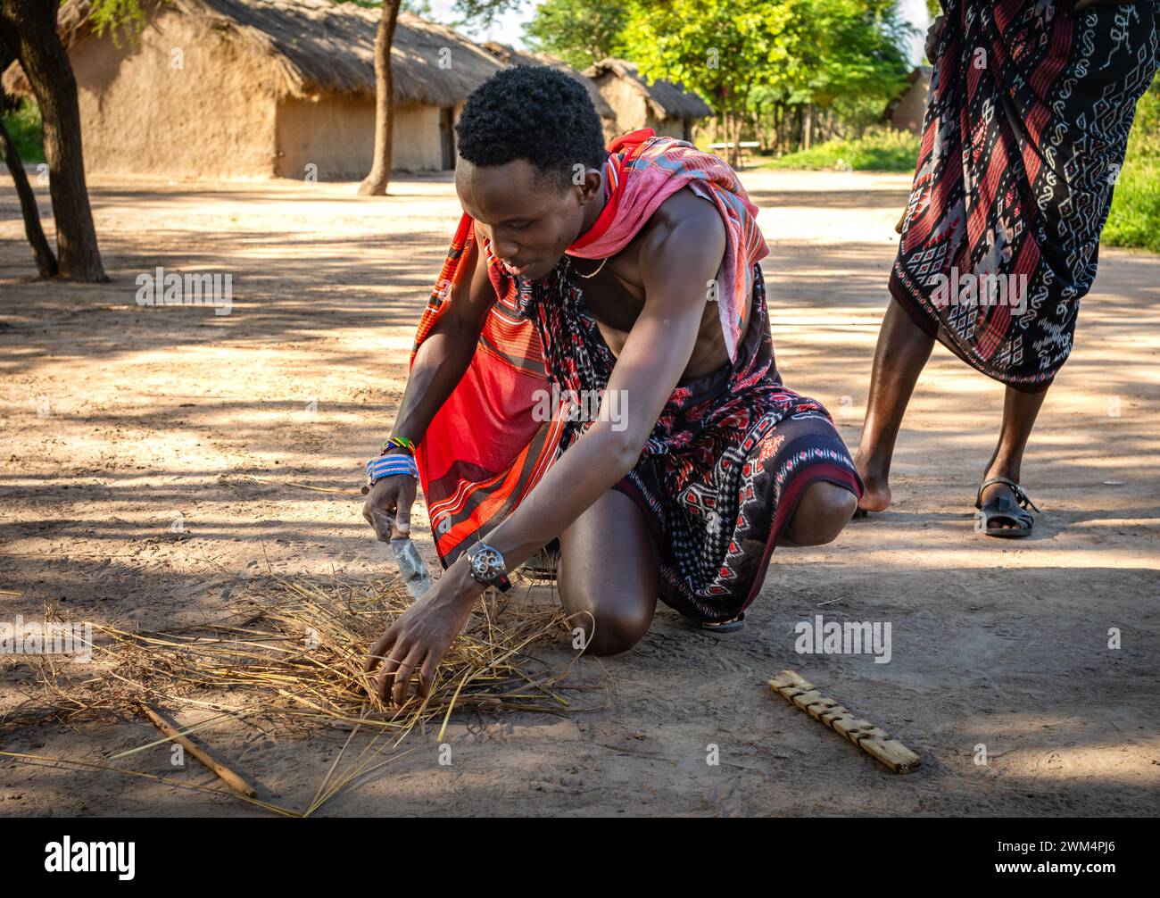 Un guerriero Maasai inizia il fuoco per attrito dopo aver sfregato i bastoni in un villaggio di Mikumi, Tanzania. Foto Stock