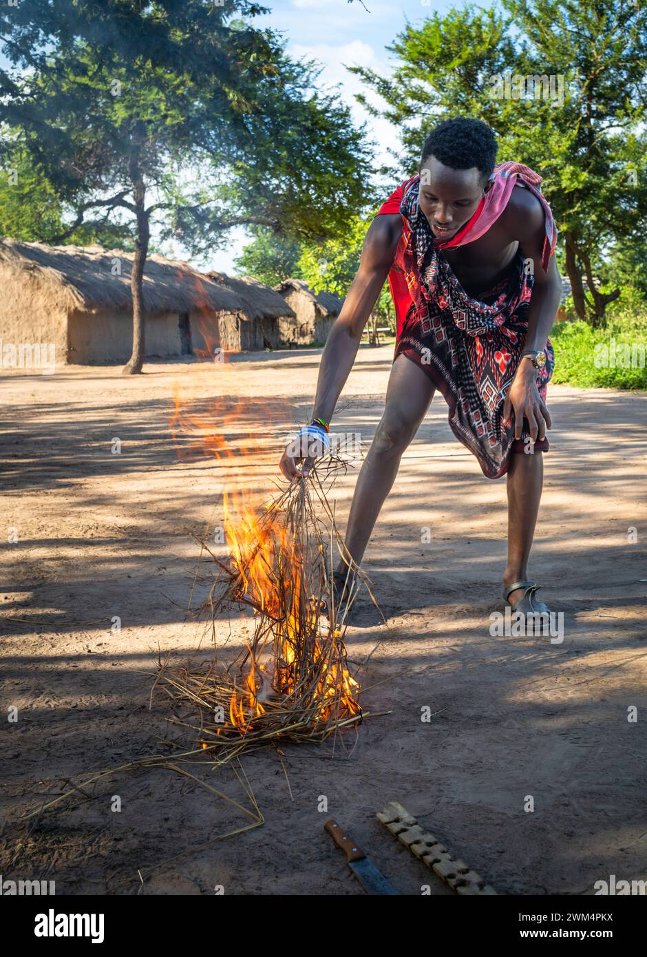 Un guerriero Maasai inizia il fuoco per attrito dopo aver sfregato i bastoni in un villaggio di Mikumi, Tanzania. Foto Stock