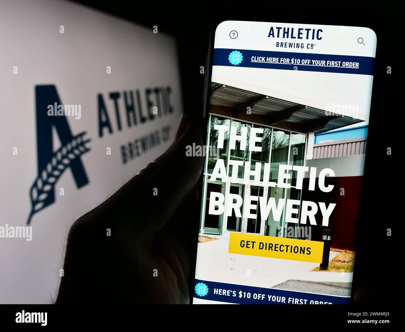 Persona che detiene un cellulare con la pagina Web della società statunitense di bevande Athletic Brewing Company davanti al logo. Messa a fuoco al centro del display del telefono. Foto Stock