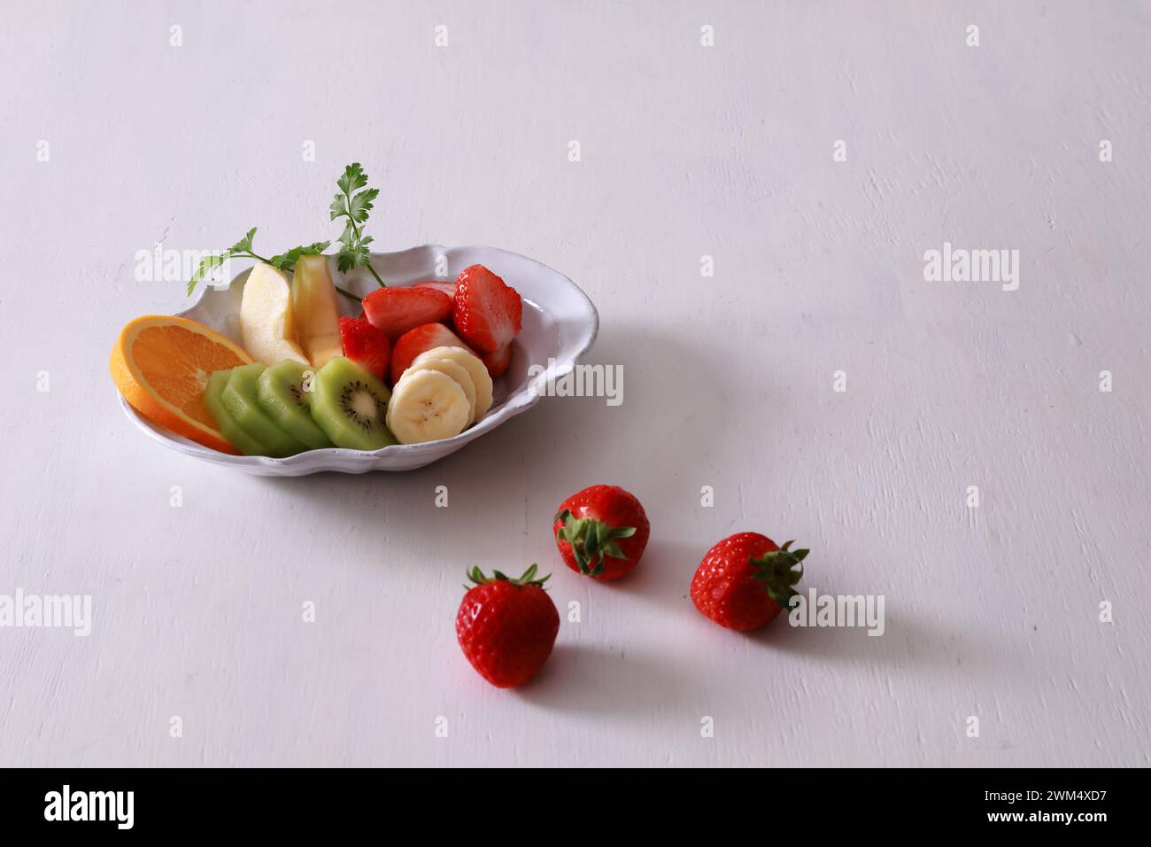 Macedonia di frutta con fragole, kiwi e banane in una ciotola su sfondo bianco Foto Stock