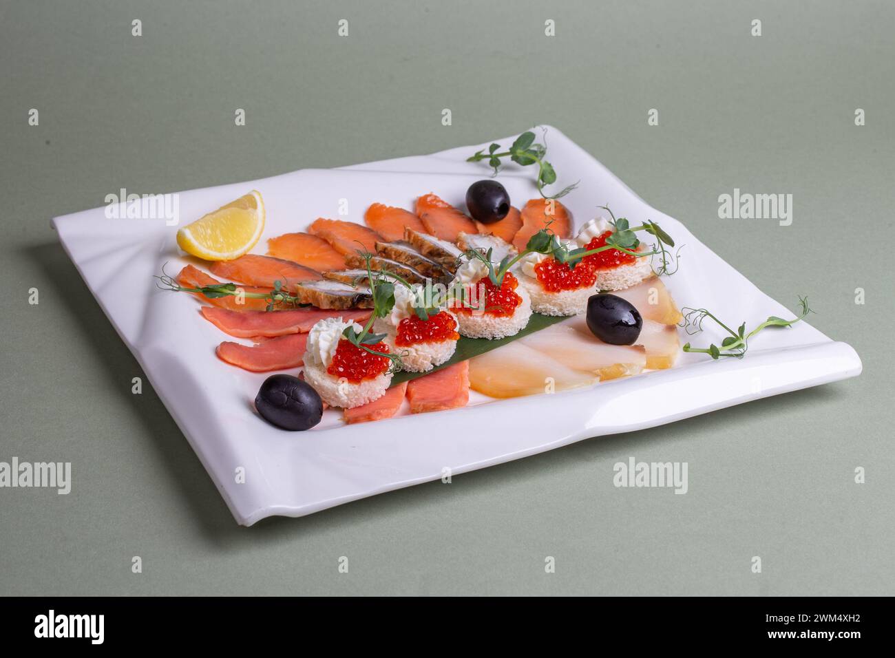 Un piatto di pesce fresco preparato ad arte - salmone, trota, caviale e gamberi - su un piatto bianco con fette di limone e verdure. Un'attrattiva visiva Foto Stock