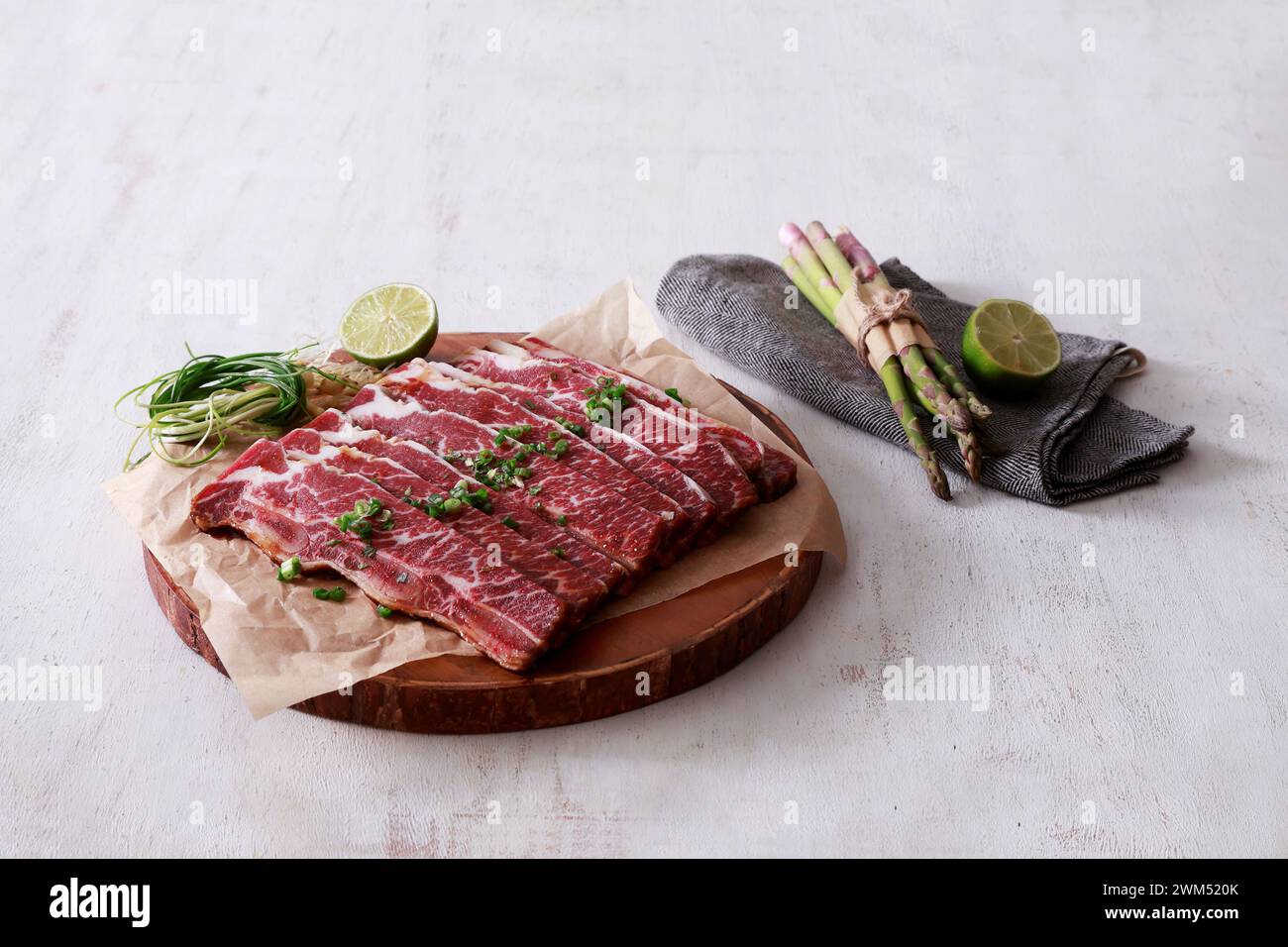 bistecca di manzo cruda con asparagi, lime ed erbe aromatiche su tavola di legno Foto Stock
