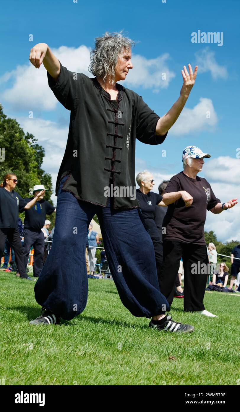 Lady in Loose Fitting Clothing insegnando Tai chi a Un gruppo di pubblico durante Una dimostrazione, mostra, Regno Unito Foto Stock