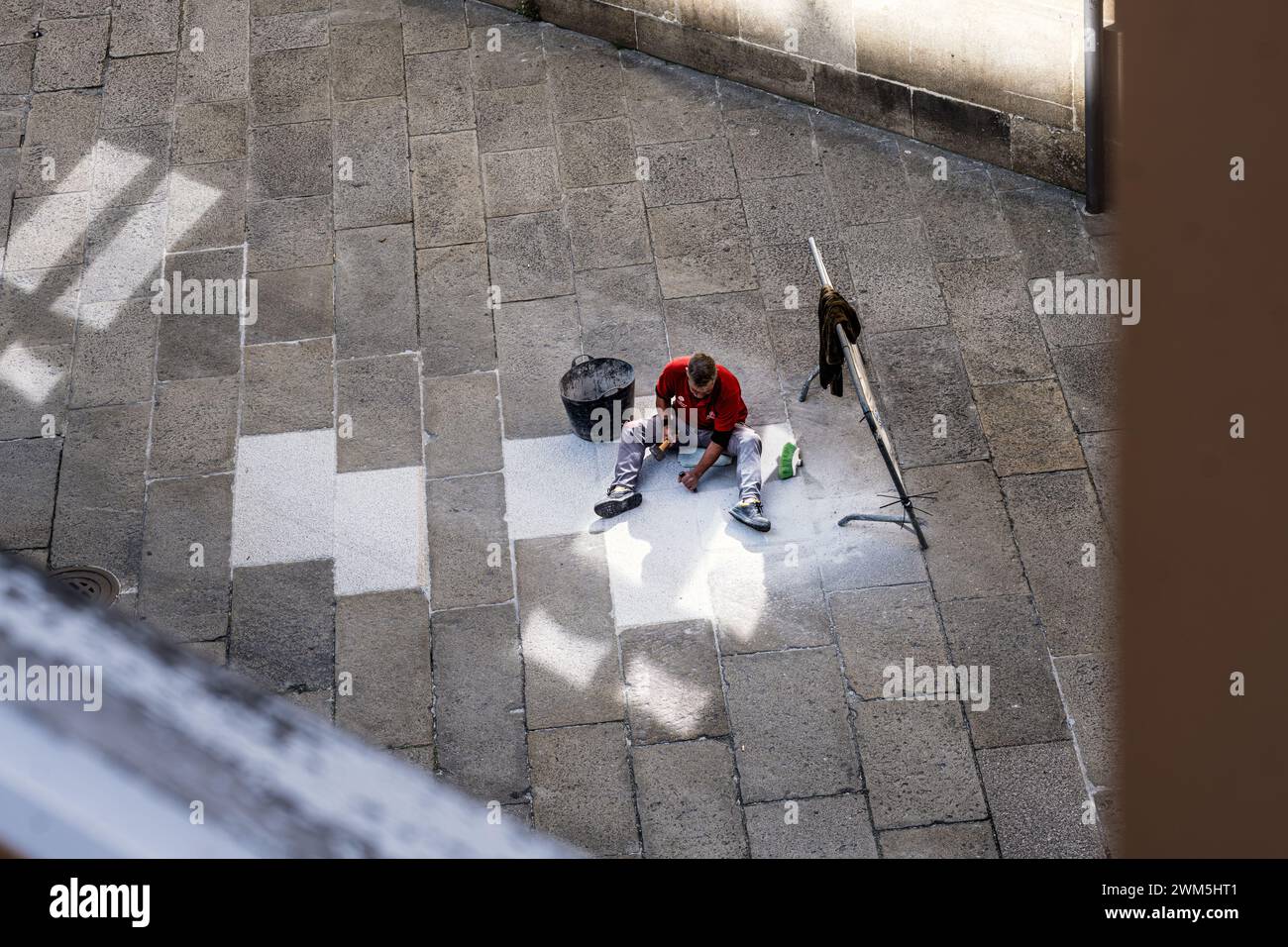 Vista dall'alto di un muratore al lavoro in una strada di pavimentazione in pietra nel centro storico di Santiago de Compostela in Spagna. Foto Stock