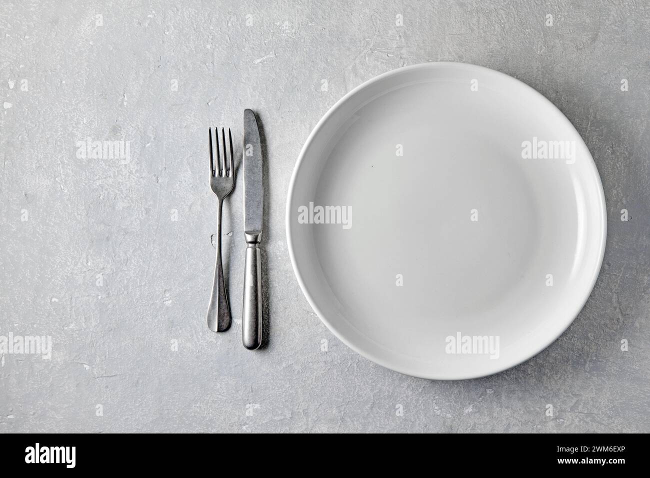 Piatto in ceramica bianca con posate su un tavolo in pietra leggera. Modello per alimenti, vista superiore con spazio di copia. Foto Stock