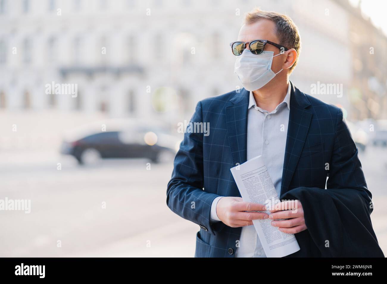 Uomo d'affari con una maschera che cammina alla luce del sole, con i documenti in mano. Foto Stock