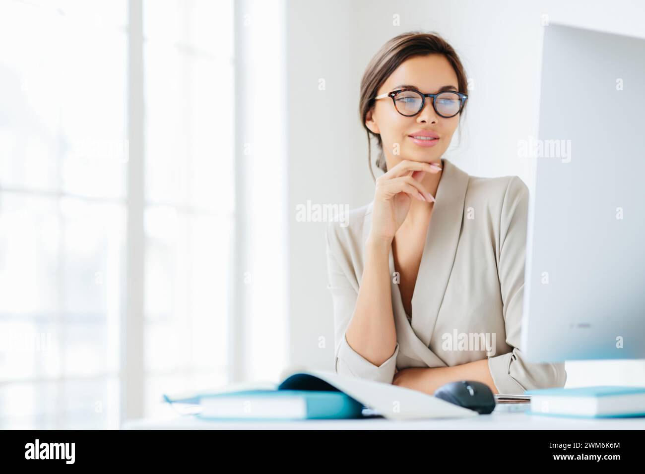 Donna d'affari contemplativa con una penna in mano, che fa una pausa attenta alla sua scrivania ben illuminata. Foto Stock