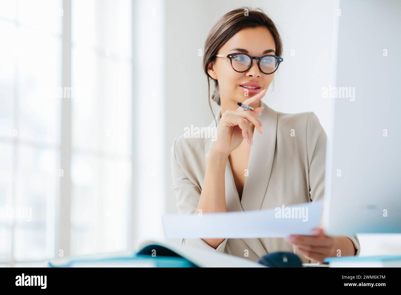 Donna d'affari con gli occhiali esamina attentamente i documenti, immersa nel lavoro. Foto Stock