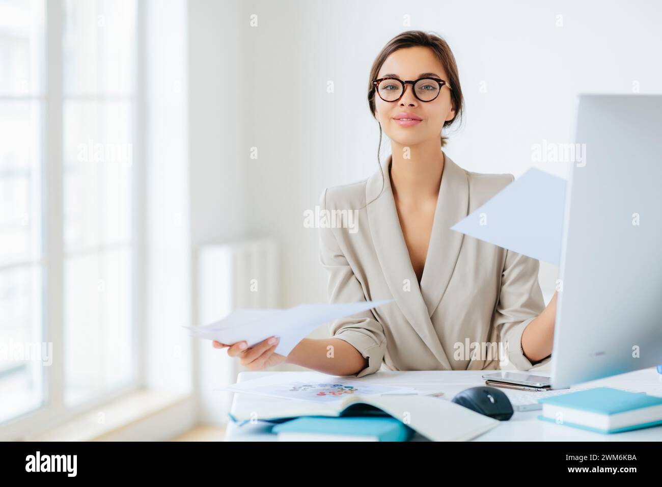 Una donna professionale trasuda fiducia, pronta a portare documenti alla scrivania illuminata dal sole. Foto Stock