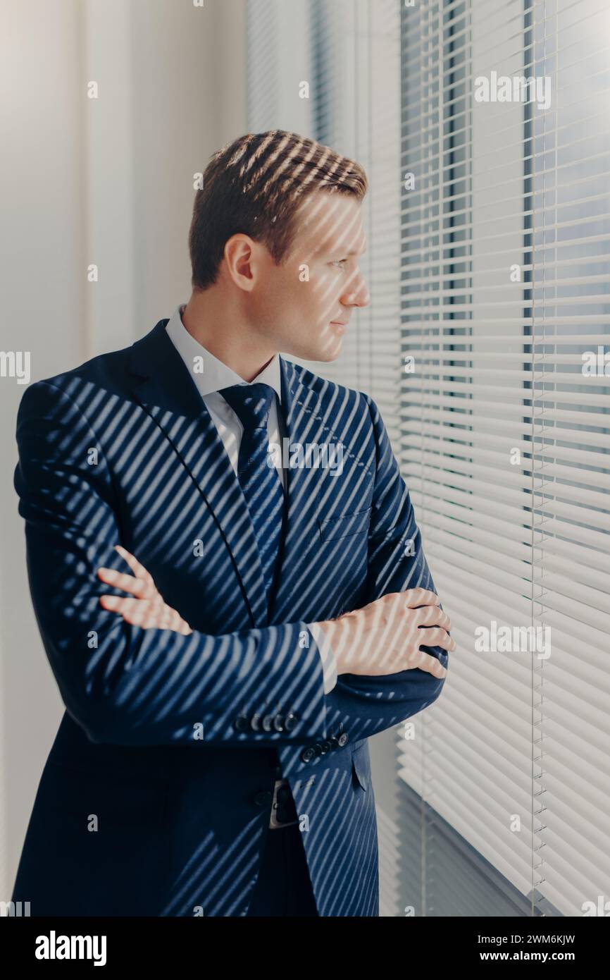 Un uomo d'affari in un ufficio illuminato dalla luce del sole contempla fuori dalla finestra. Foto Stock