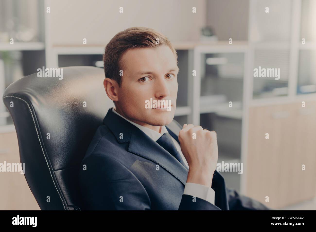 Uomo d'affari sicuro di sé che posa con un'espressione premurosa in un ufficio elegante. Foto Stock