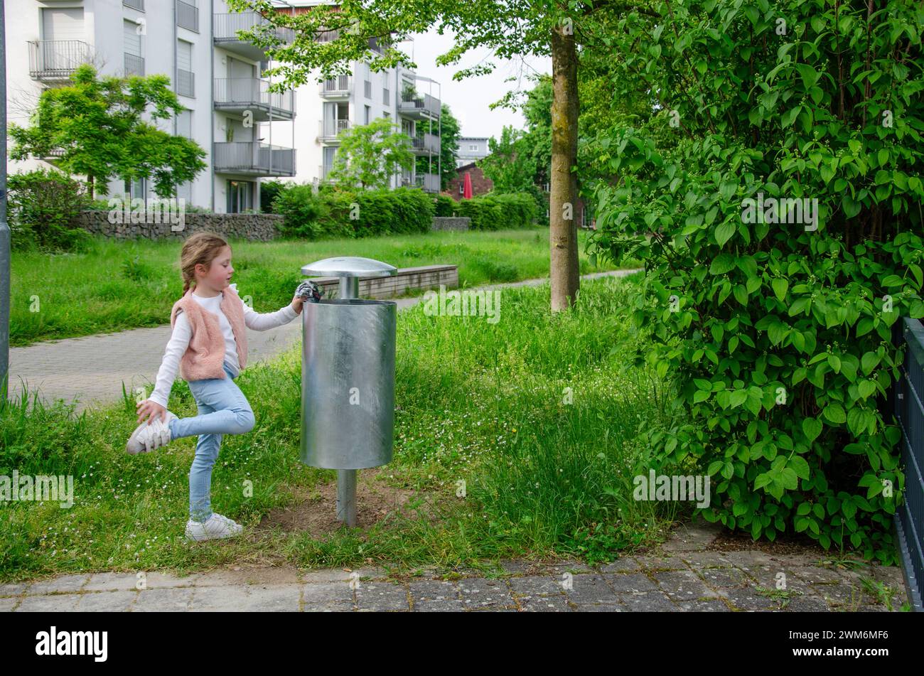 Una ragazza getta la spazzatura in un bidone della spazzatura. Foto Stock