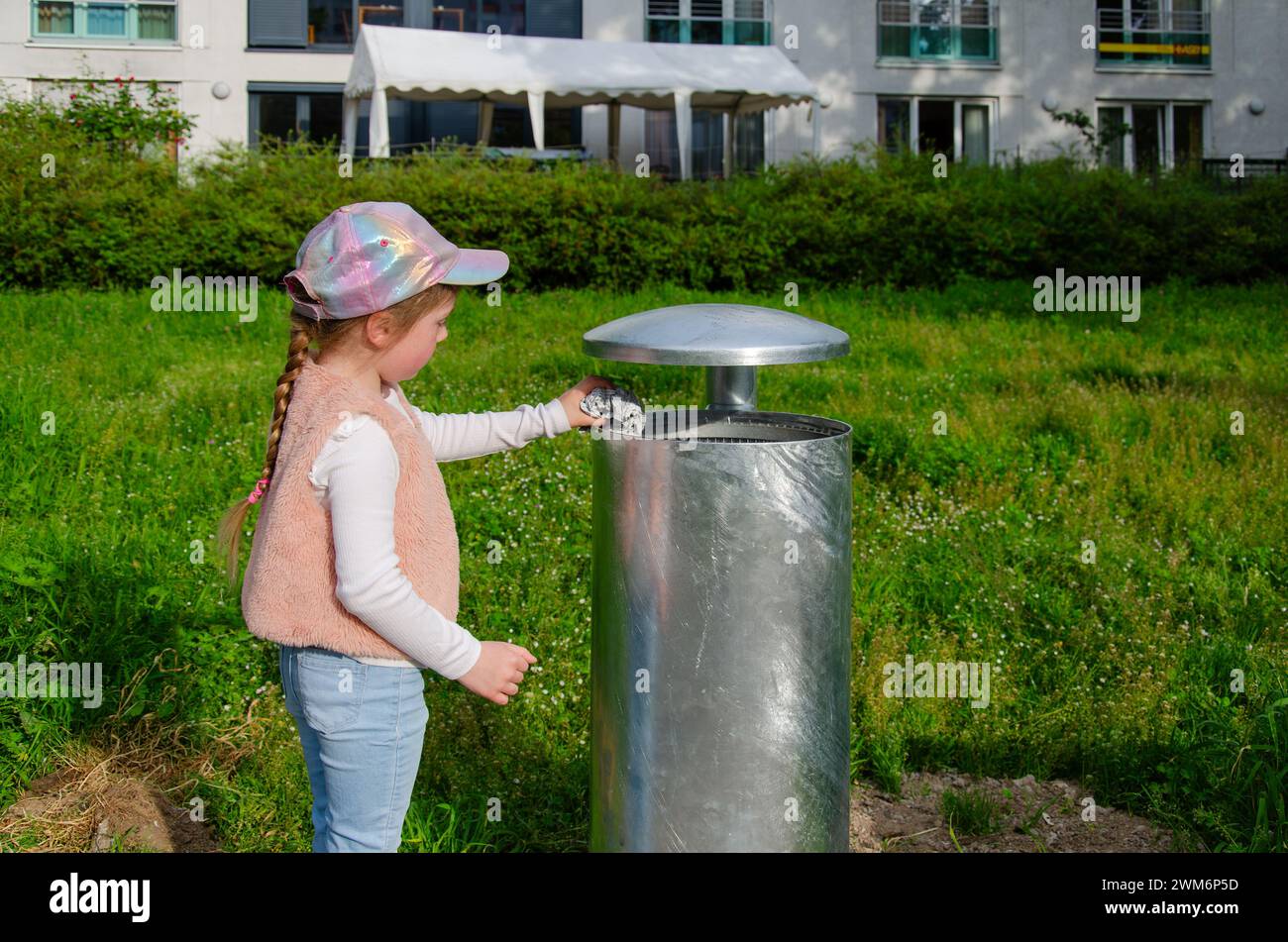 Una ragazza getta la spazzatura in un bidone della spazzatura. Foto Stock