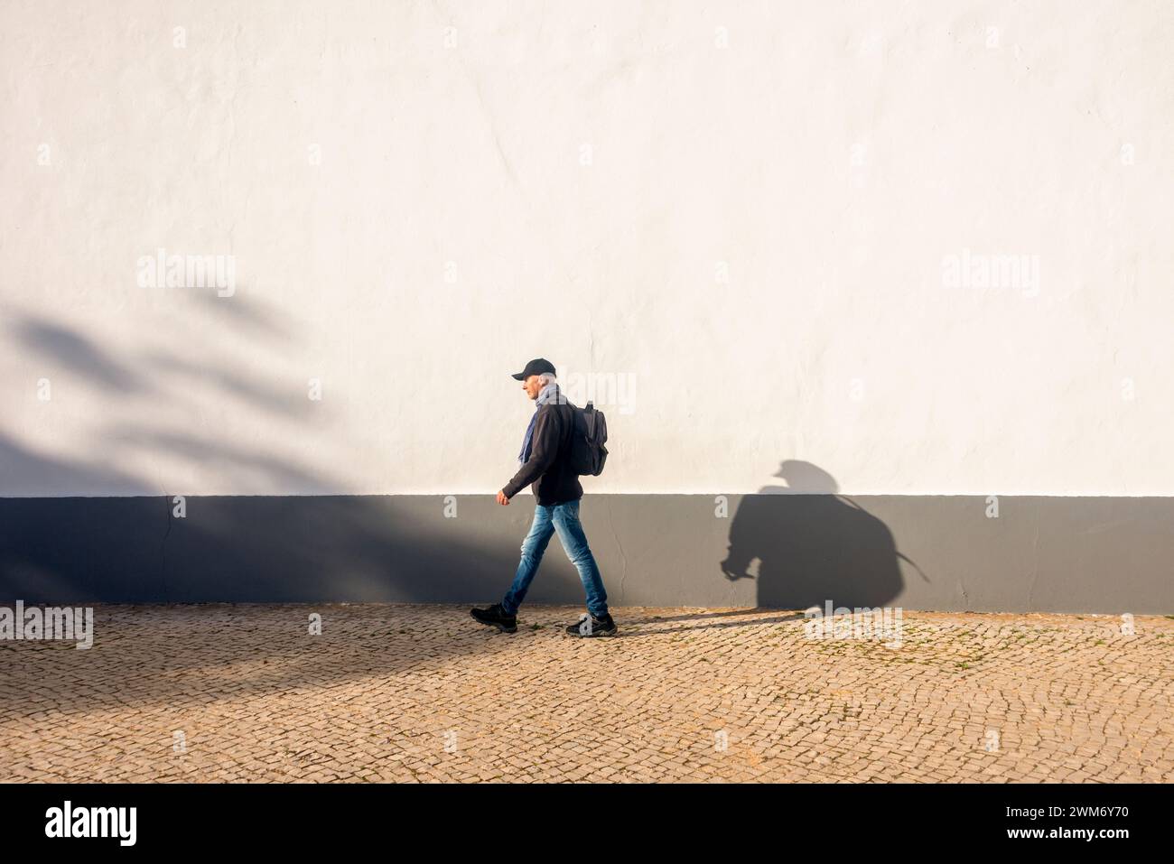 uomo con uno zaino che cammina accanto a un muro bianco, esercizio fisico. Foto Stock