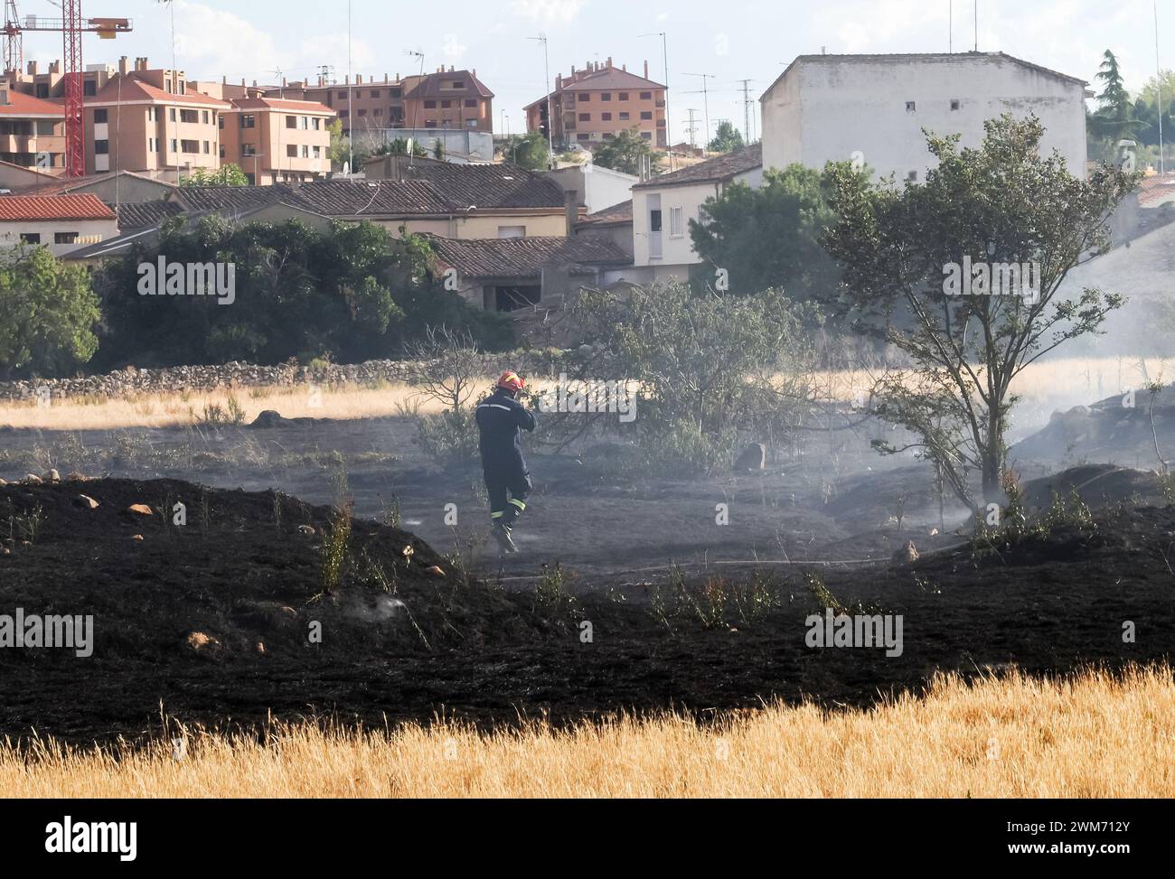 Un vigile del fuoco cammina attraverso il fumo sull'erba bruciata dopo un incendio in un campo cittadino. Foto Stock