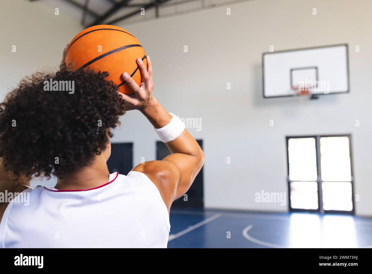 Il giovane uomo birazziale si prepara a sparare a un pallacanestro in una palestra coperta con spazio per copiare Foto Stock