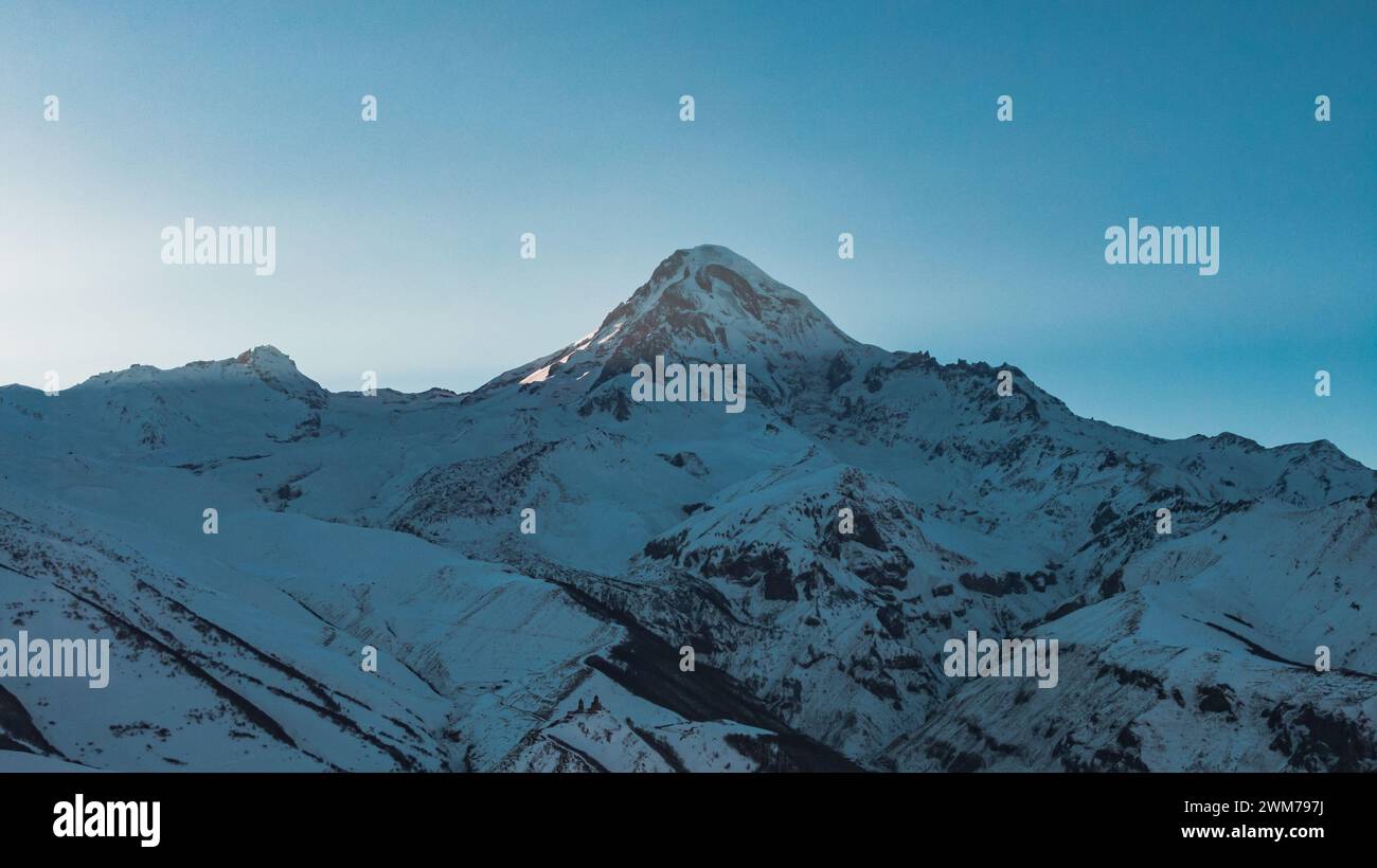 L'ultima luce del tramonto illumina la vetta di una montagna innevata, emettendo un leggero bagliore sul terreno accidentato. La scena è una tranquilla dimostrazione della maestosa presenza della montagna. Foto Stock