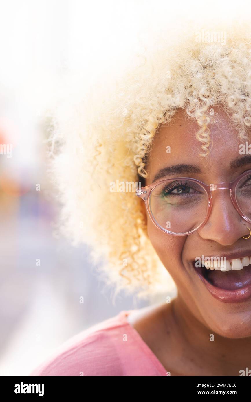 La giovane donna birazziale sorride brillantemente in un ambiente all'aperto illuminato dal sole della città Foto Stock