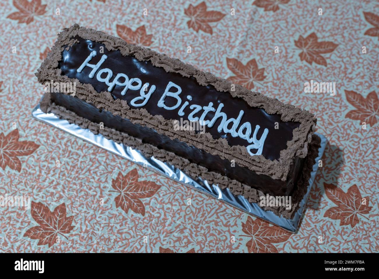 Delizia celebrativa. Torta al cioccolato con condimento di lettere bianche per buon compleanno. Tema autunnale, tabella fogli. Foto Stock