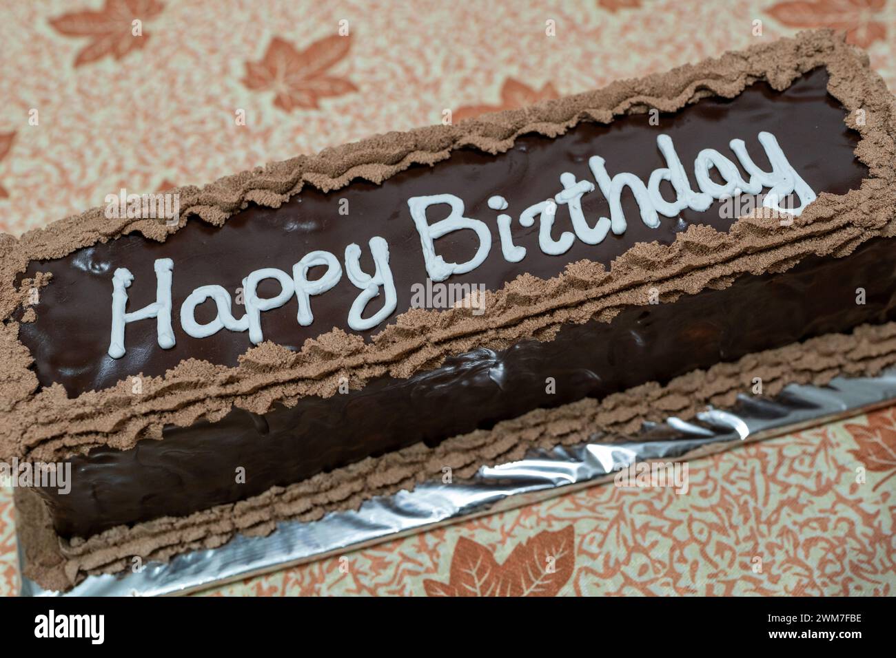 Delizia celebrativa. Torta al cioccolato con condimento di lettere bianche per buon compleanno. Tema autunnale, tabella fogli. Foto Stock