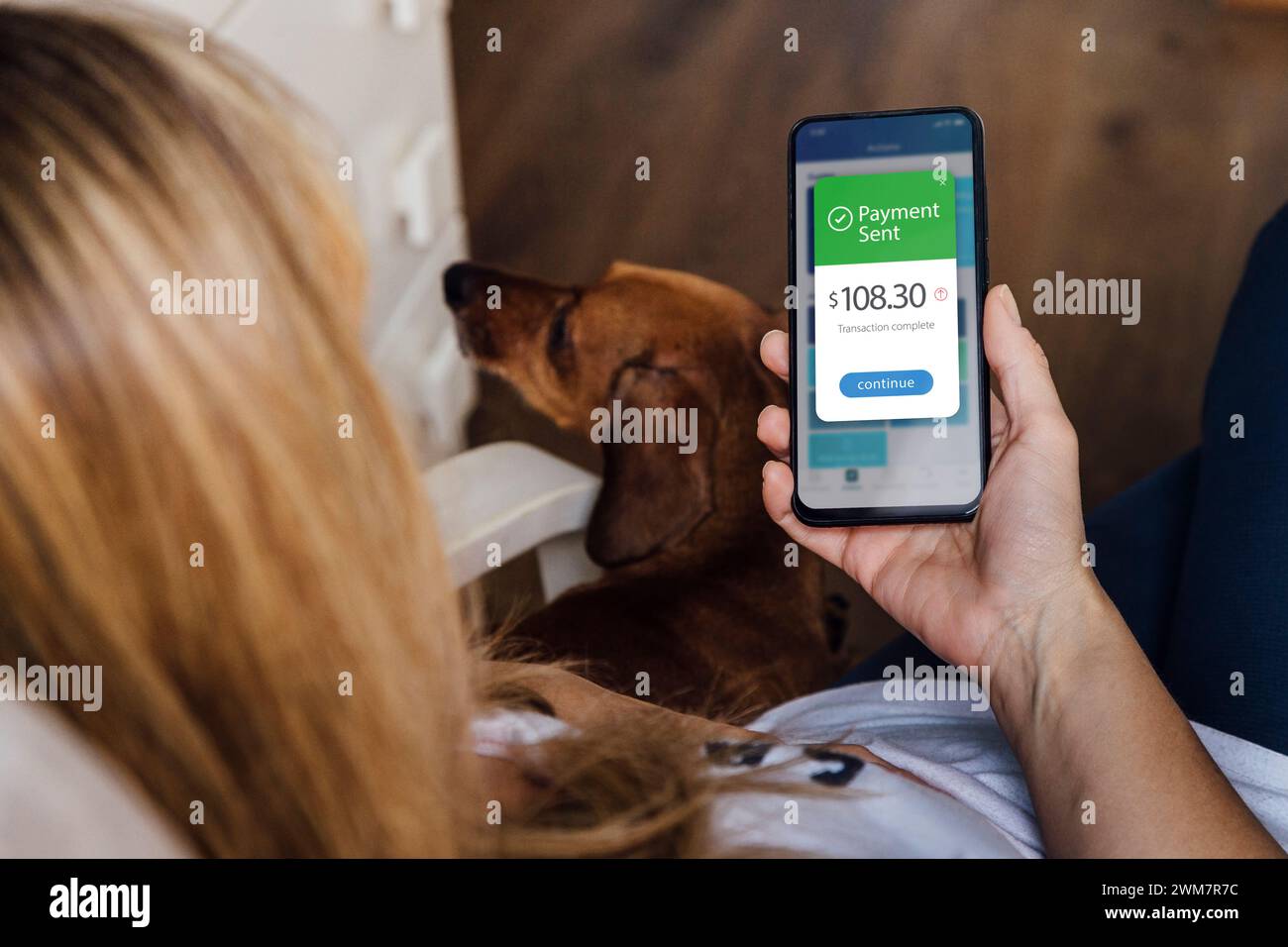 Telefono cellulare con un'applicazione finanziaria sullo schermo. Rilassa la donna con il suo cane, trasferisce denaro online utilizzando le applicazioni per inviare e ricevere valuta. Foto Stock