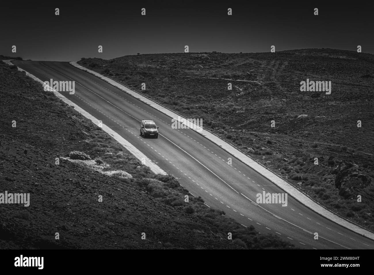 Monovolume che viaggia su una strada vuota attraverso il deserto di sabbia nera a Lanzarote Foto Stock