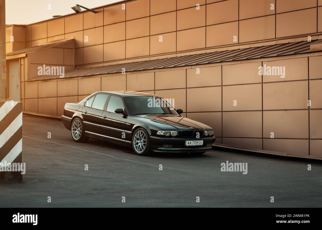 Berlina nera BMW serie 7 (E38) parcheggiata vicino alla parete marrone-bronzo beige. Vista frontale di tre quarti dell'auto executive degli anni '1990. Foto Stock