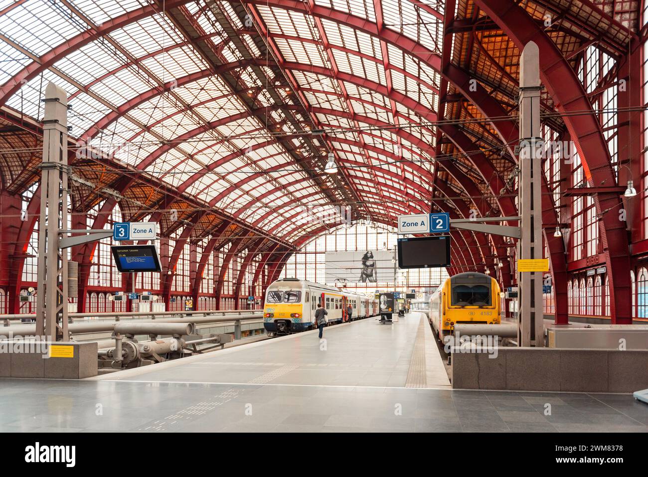 Sala dei treni della stazione centrale di Anversa. Vista di alcune piattaforme all'interno di un grande capannone arioso con travi in metallo color Bordeaux Foto Stock