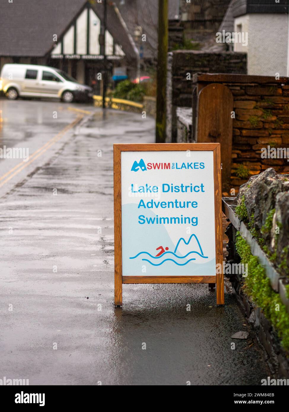 Una "nuotata nei laghi" Una tavola che pubblicizza il Lake District Adventure nuotando sul marciapiede ironicamente in una giornata molto piovosa e umida. Foto Stock