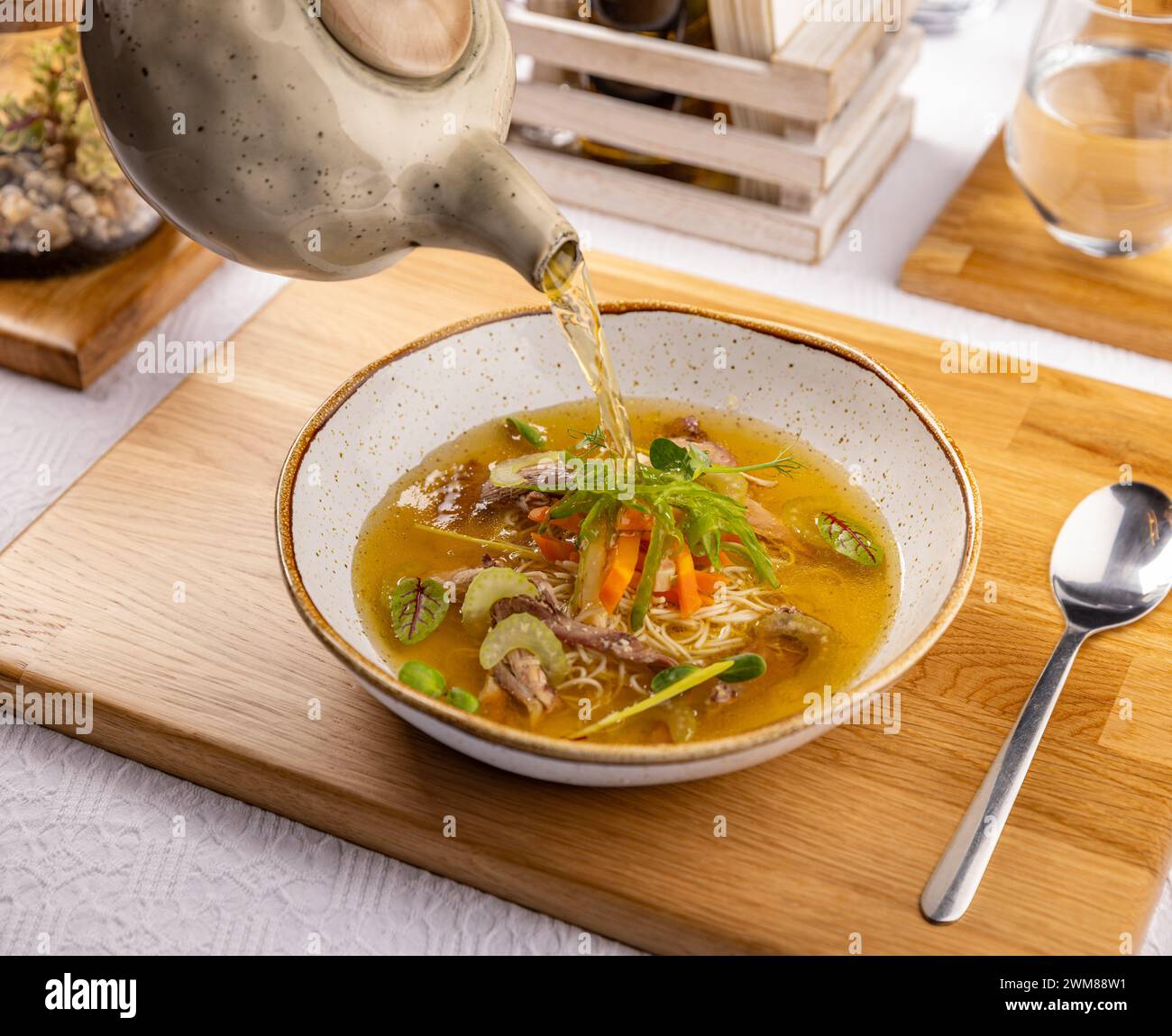 Il cameriere versa il brodo in una zuppa di pollo con spaghetti, carne e verdure. Foto Stock