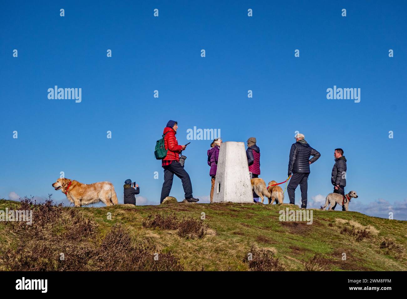 Le persone che camminano cani si sono fermate per parlare e ammirare la vista dal trig point di Eyam Moor sopra il villaggio di Eyam nel Derbyshire Peak District Foto Stock