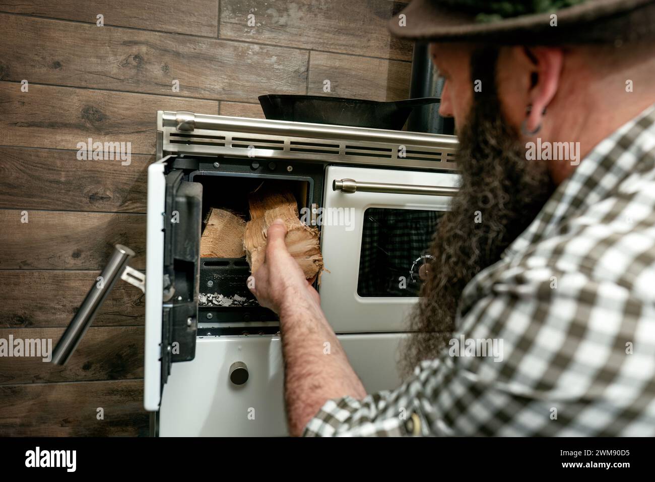 Un uomo bavarese con barba che riscalda una stufa a legna vintage Foto Stock