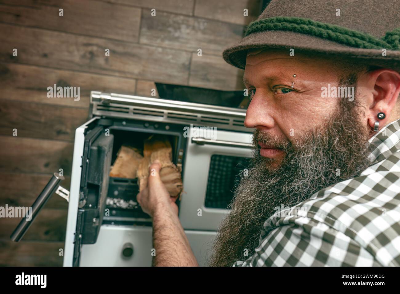 Un uomo bavarese con barba che riscalda una stufa a legna vintage Foto Stock