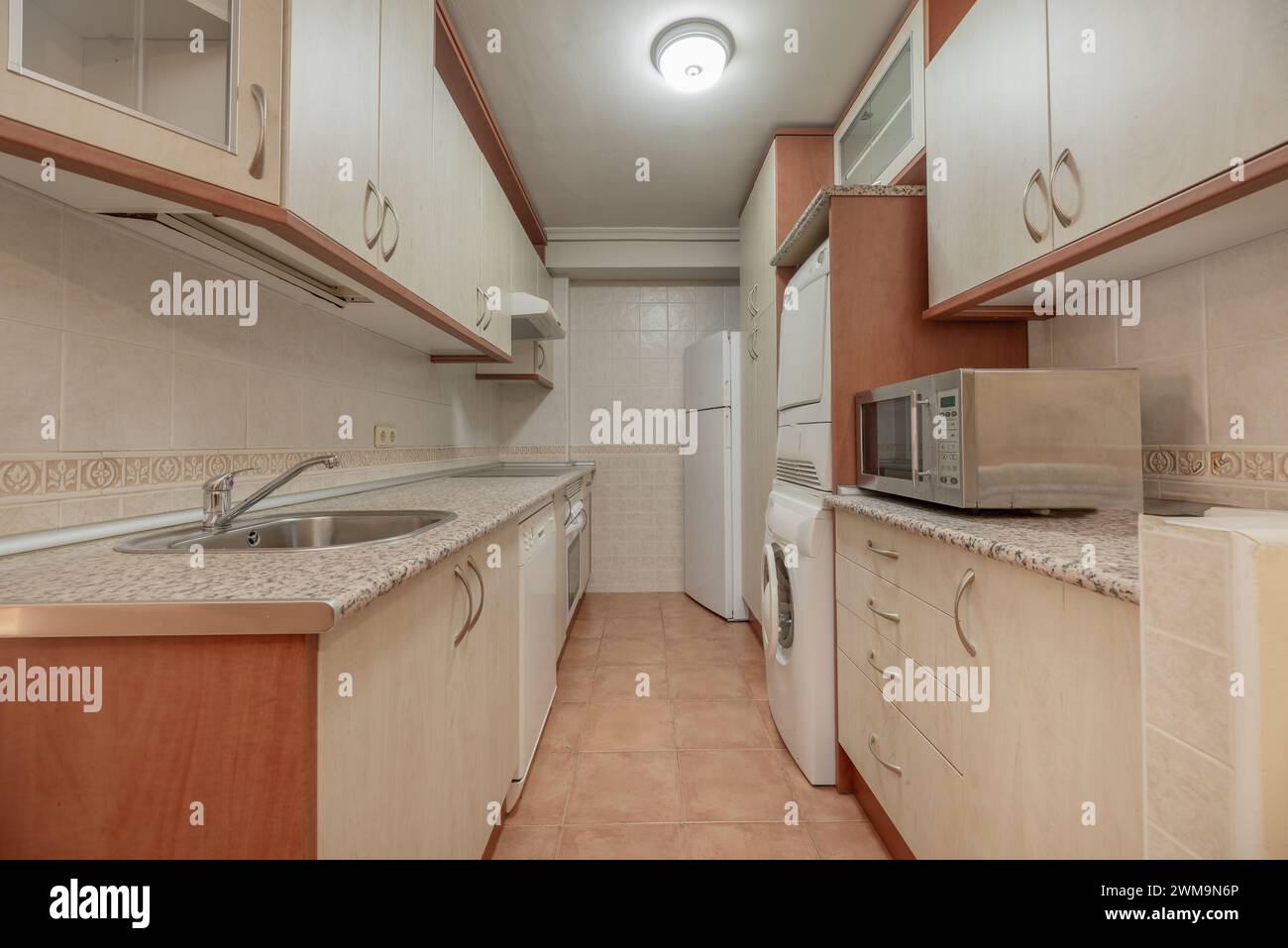 Cucina attrezzata arredata con mobili color crema, elettrodomestici bianchi e pavimenti in gres marrone chiaro Foto Stock