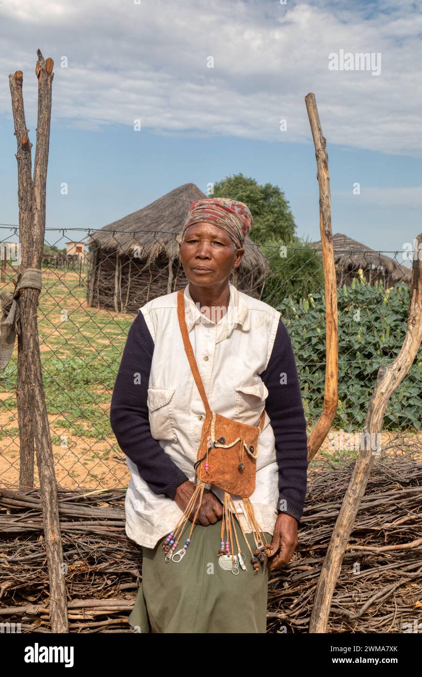 vecchia donna africana del villaggio nel cortile, con borsa tradizionale, in baita sullo sfondo con tetto di paglia e cielo blu, sud africa Foto Stock