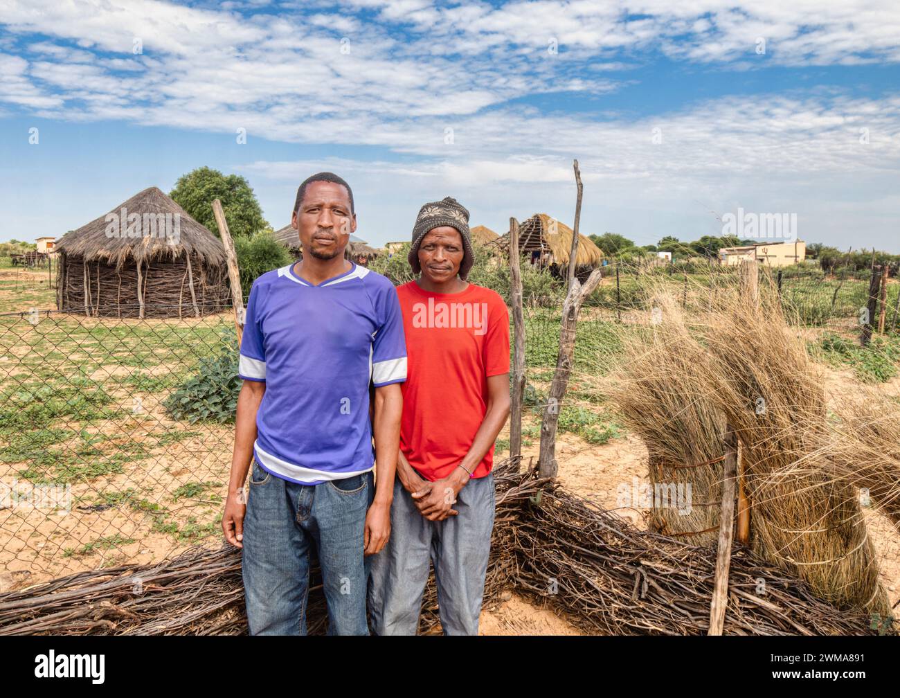 villaggio due uomini africani nel cortile, sullo sfondo capanna con tetto di paglia e cielo blu, sud africa Foto Stock