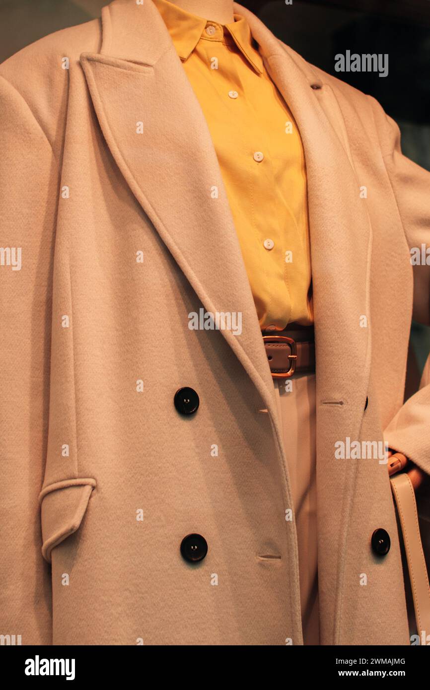 Primo piano di un cappotto lungo beige e di una camicia gialla brillante. Moda casual ed elegante da donna Foto Stock