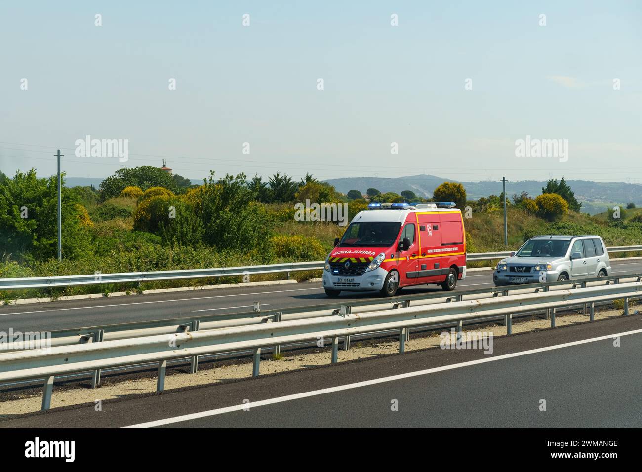 Marguerite, Francia - 16 maggio 2023: Un'ambulanza rossa viene catturata in movimento guidando lungo un'autostrada a più corsie con un cielo azzurro limpido sopra la testa e il verde Foto Stock