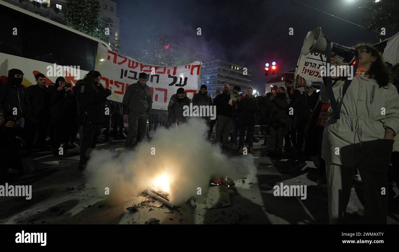 La polizia spegne un falò acceso dai manifestanti durante una manifestazione nei pressi della residenza ufficiale del primo ministro che chiede il rilascio degli ostaggi detenuti da Hamas nella Striscia di Gaza il 19 febbraio 2024 a Gerusalemme. Israele Foto Stock