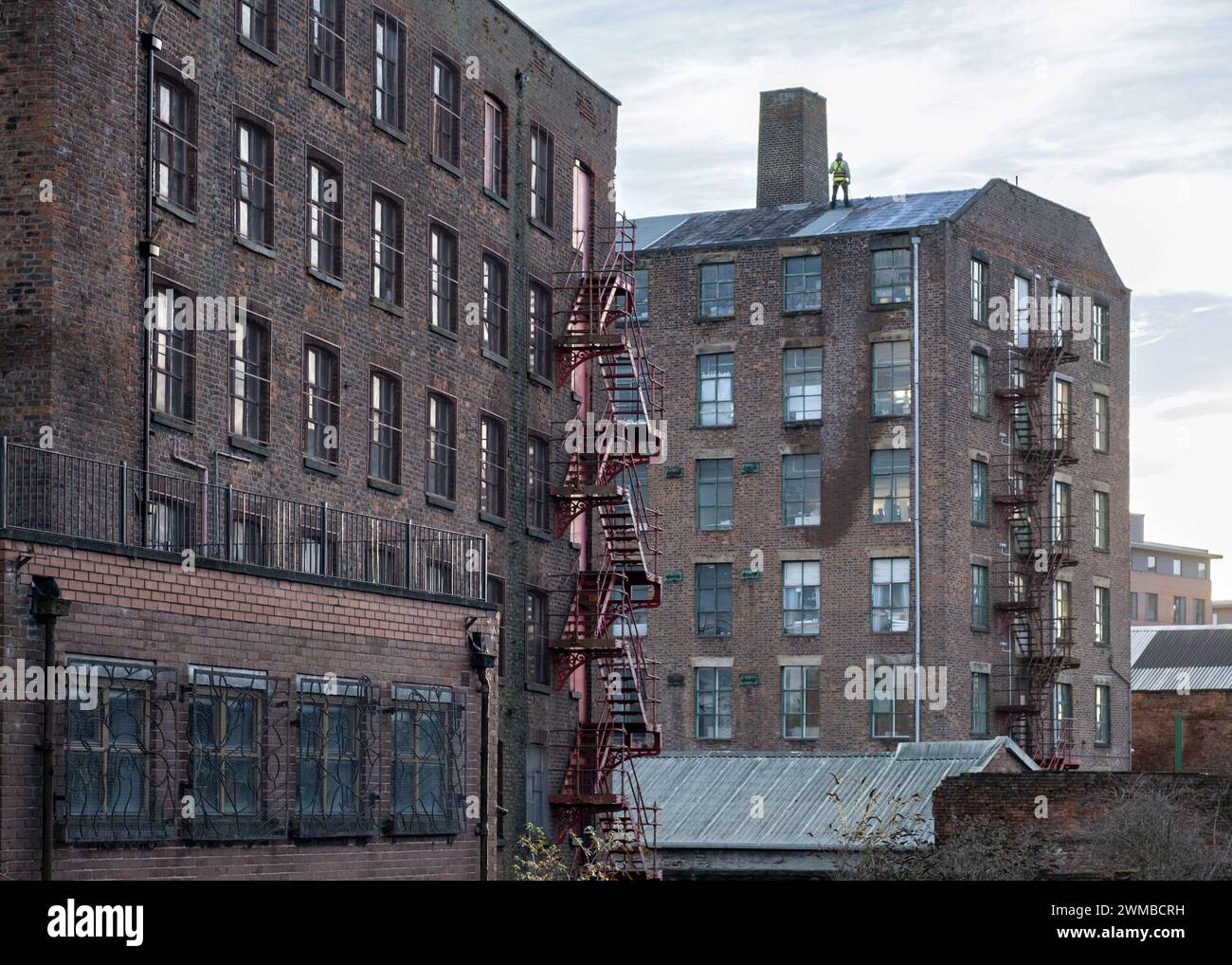 Vecchio mulino di Manchester / edifici di magazzino lungo il canale. I gradini di fuga possono essere visti all'esterno, un uomo lavora sul tetto. Foto Stock