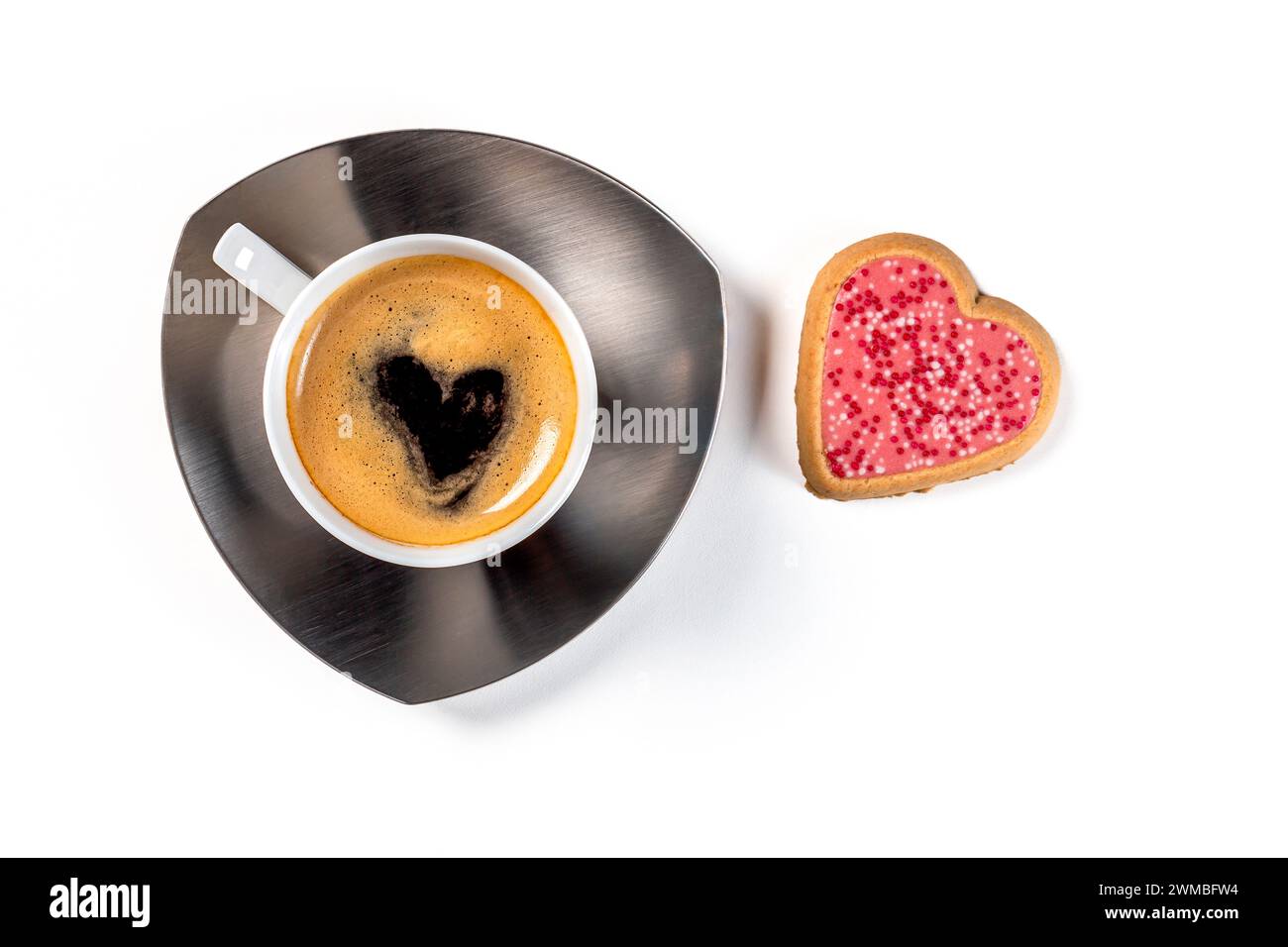 Una tazza di caffè su un piattino con un biscotto a forma di cuore in glassa rosa. Vista dall'alto su sfondo bianco. Foto Stock