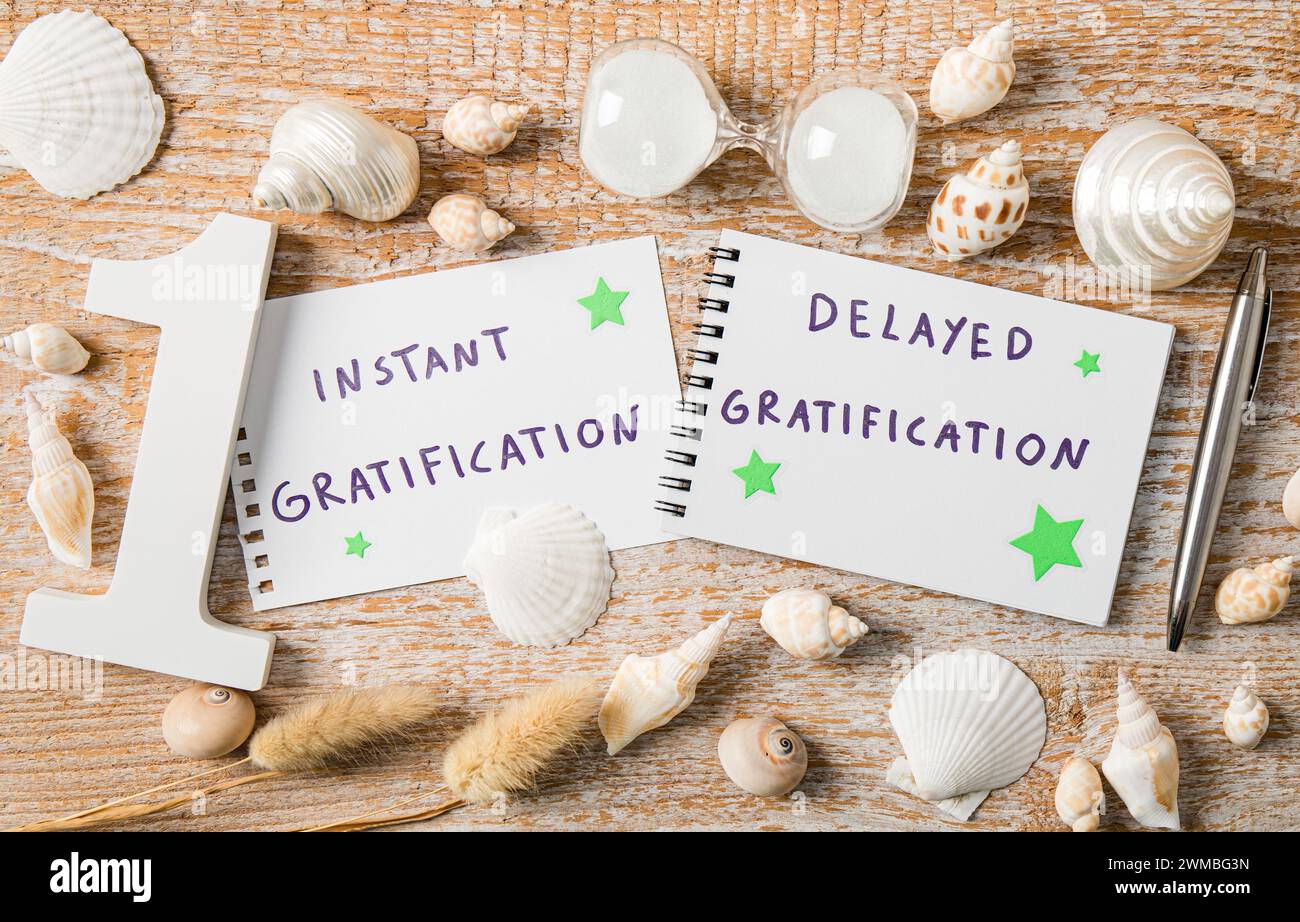 Concetto di gratificazione immediata contro gratificazione ritardata. Testo su carta decorato con conchiglie in studio al chiuso. Foto Stock