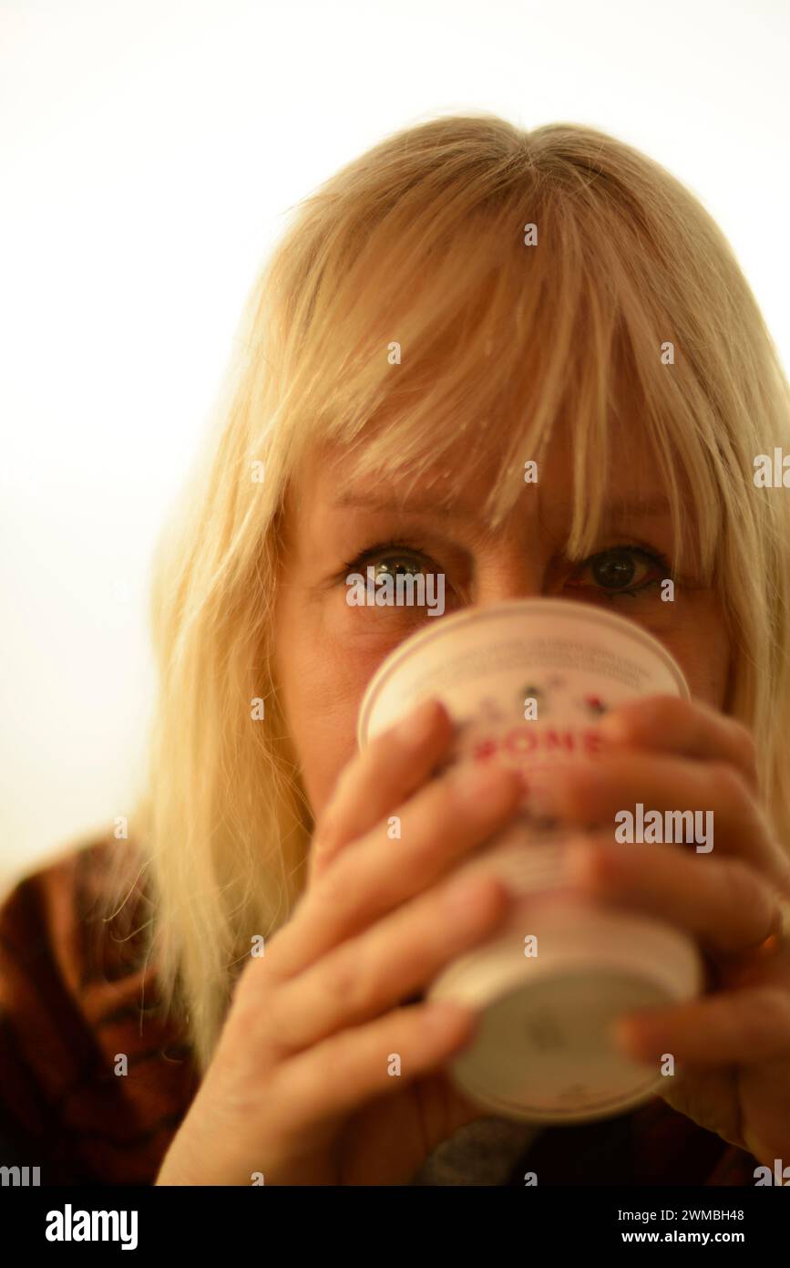 Donna che beve caffè da una tazza usa e getta o riciclabile, primo piano, concentrati sugli occhi Foto Stock
