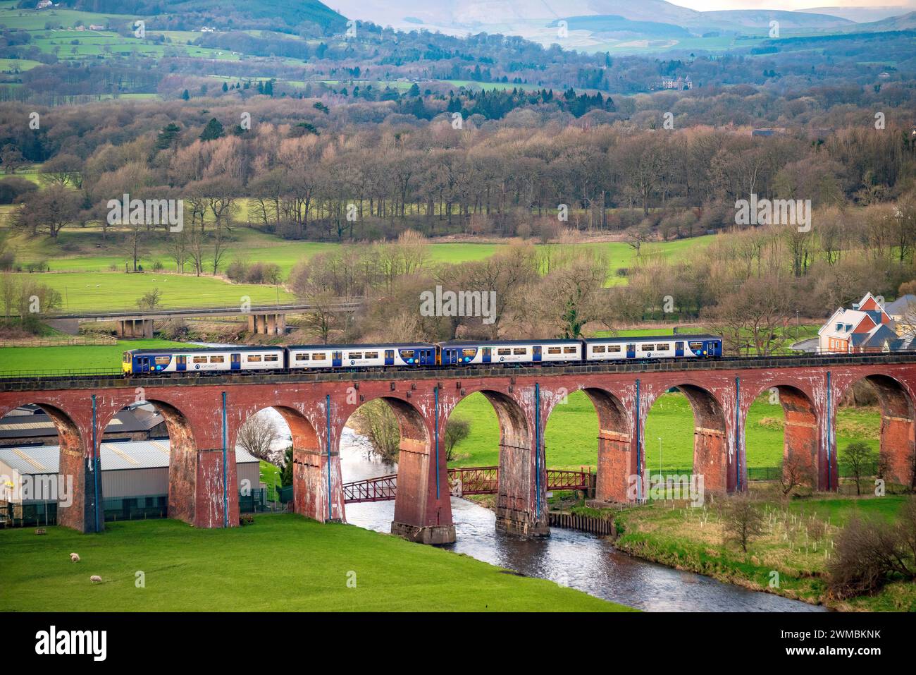 Un treno diesel della Northern Rail visto qui che attraversa il viadotto Whalley Arches sul fiume Calder alla luce della sera. Foto Stock