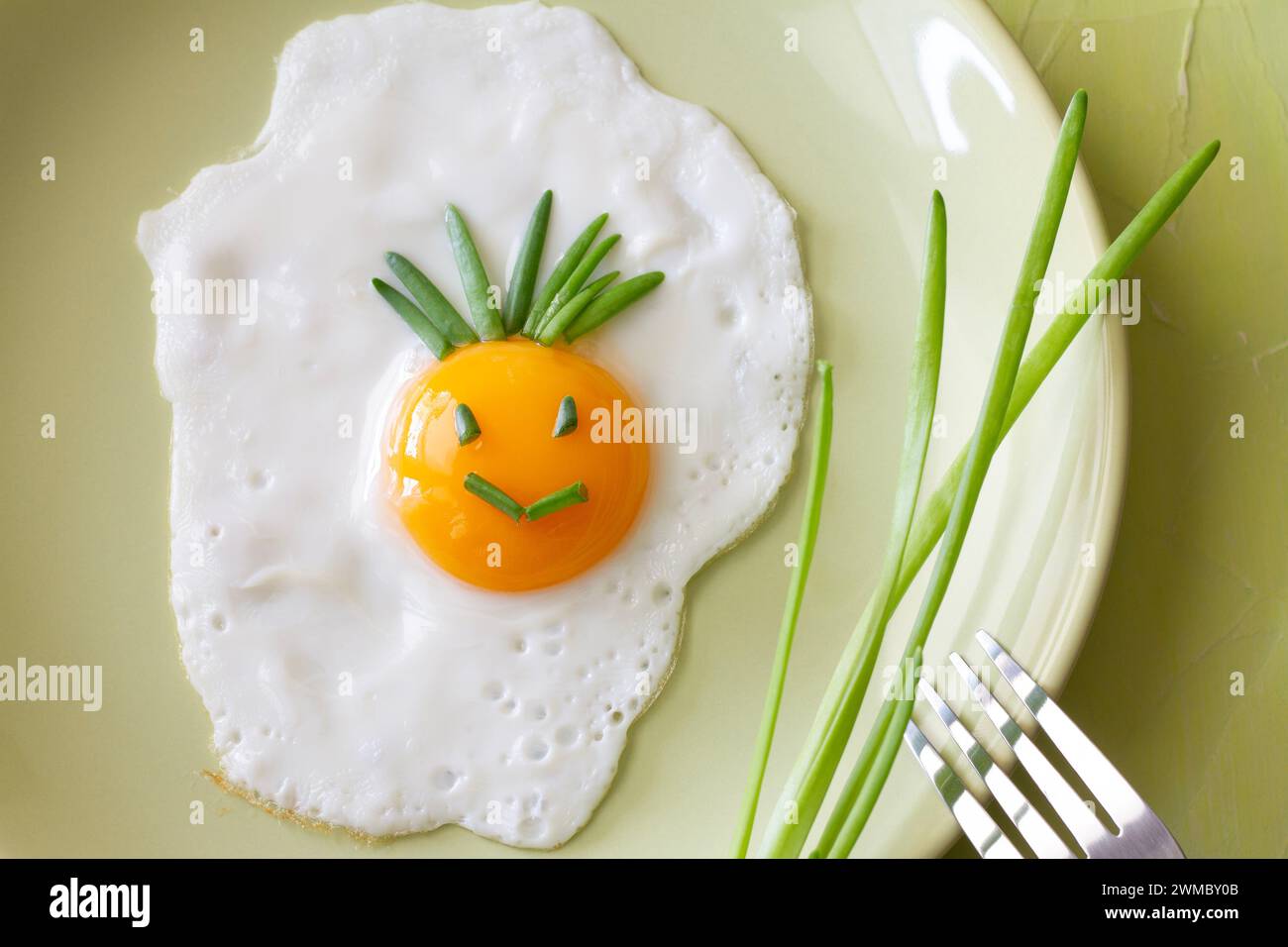 Divertente uovo fritto con sorriso sorridente sul piatto con erba cipollina, concetto creativo per la colazione Foto Stock